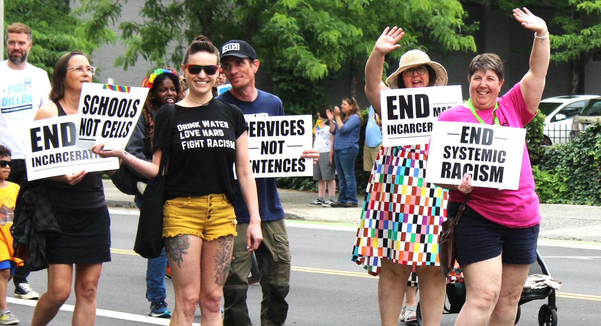 Image of multiple people marching in 2023 spokane pride parade with signs that read "end systemic racism", "end mass incarceration", "services not sentences", and more