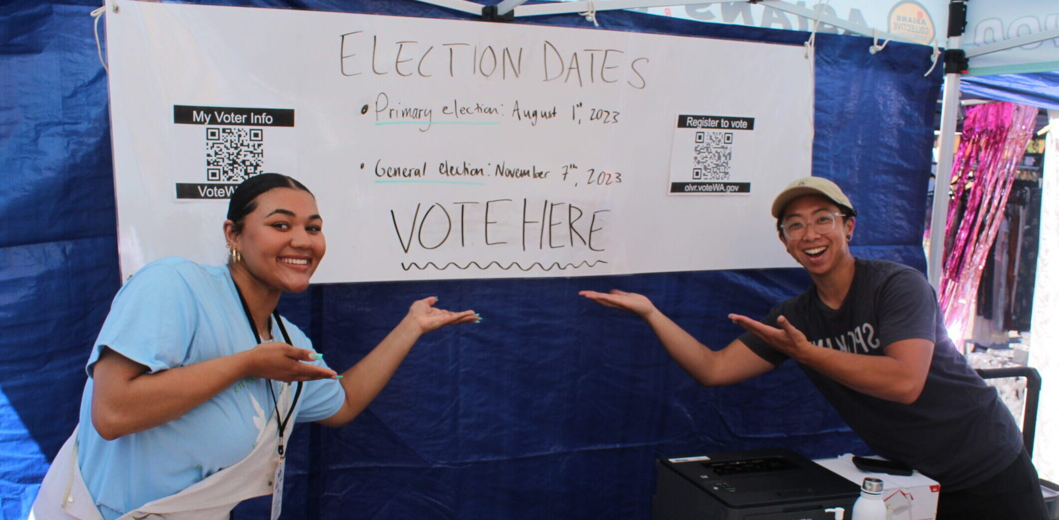 Image of 2 people standing in front of a sign intended to get out the vote.